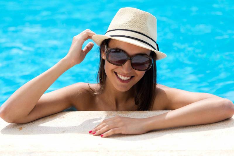 femme brune avec un chapeau d'été qui s'accoude à la margelle dans une piscine à Toulon