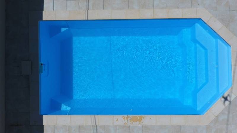 Piscine coque polyester Lazuli 7m à fond plat – escalier central et banquette intégrée.